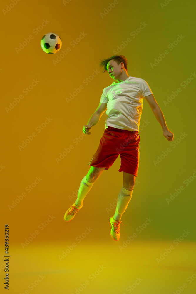 Young caucasian man, male soccer football player training isolated on gradient yellow green background in neon light
