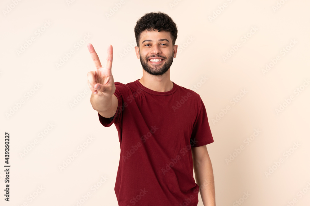 Young Moroccan man isolated on beige background smiling and showing victory sign Young Moroccan man isolated on beige background smiling and showing victory sign