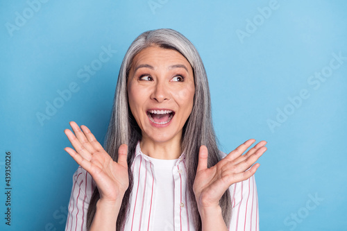 Photo of aged woman happy positive simile amazed surprised news sale look empty space isolated over blue color background photo