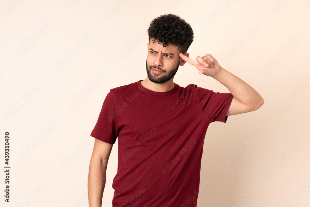 Young Moroccan man isolated on beige background making the gesture of madness putting finger on the head Young Moroccan man isolated on beige background making the gesture of madness putting finger on the head