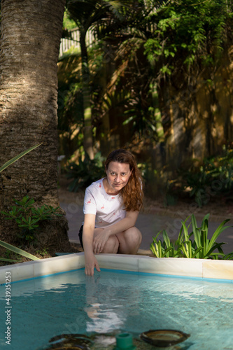 Retrato vertical de una mujer caucasiana joven guapa tocando el agua de una piscina
