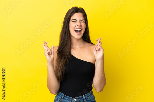 Young Brazilian woman isolated on yellow background with fingers crossing