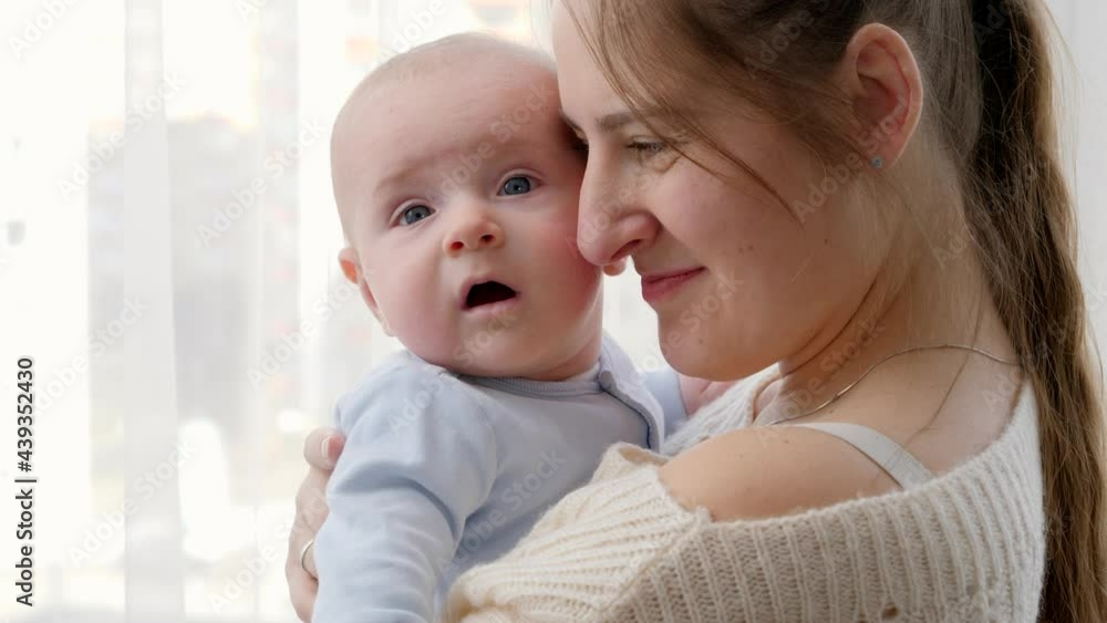 Closeup portrait of baby and mother face hugging and embracing at big window at home. Concept of family happiness and child development Closeup portrait of baby and mother face hugging and embracing at big window at home. Concept of family happiness and child development