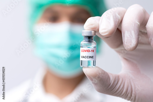 Doctor wears face mask and white medical glove hand holding flu, coronavirus, covid-19 liquid vaccine vial bottle preparing for injection. Vaccination for fight Covid-19 virus concept.