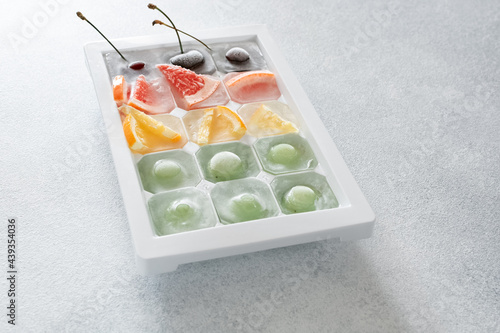 various pieces of fruit and berries frozen in ice lie in a tray on a light stone table