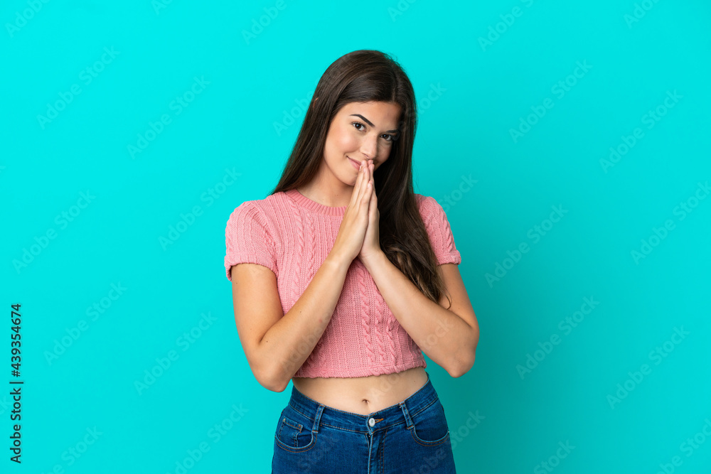 Young Brazilian woman isolated on blue background keeps palm together. Person asks for something Young Brazilian woman isolated on blue background keeps palm together. Person asks for something