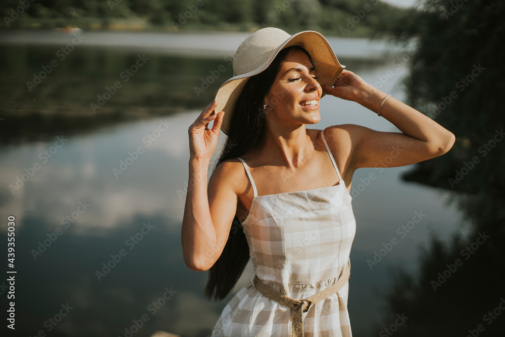 Relaxing young woman standing on wooden pier at the lake