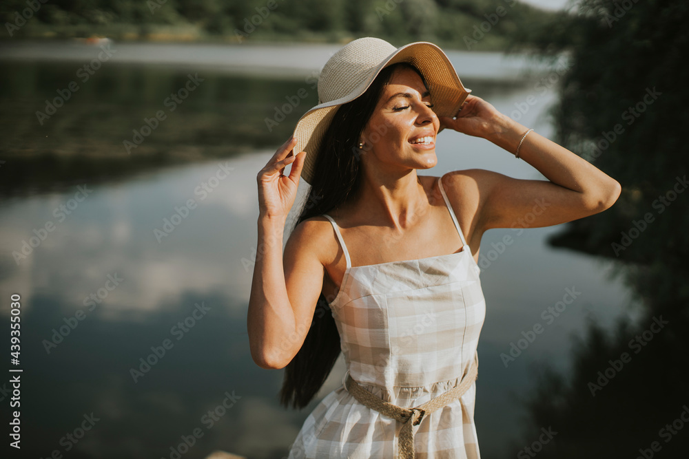 Fototapeta premium Relaxing young woman standing on wooden pier at the lake