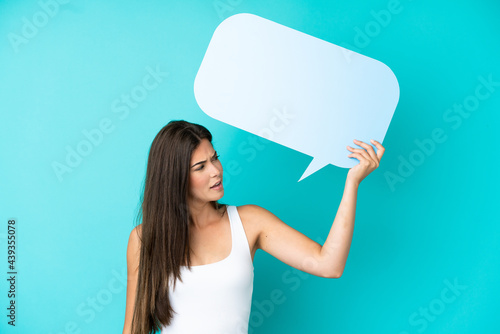 Young Brazilian woman isolated on blue background holding an empty speech bubble and with sad expression