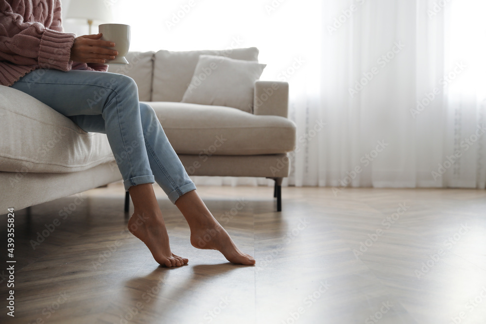 Barefoot woman sitting on sofa in living room, closeup. Floor heating system Barefoot woman sitting on sofa in living room, closeup. Floor heating system