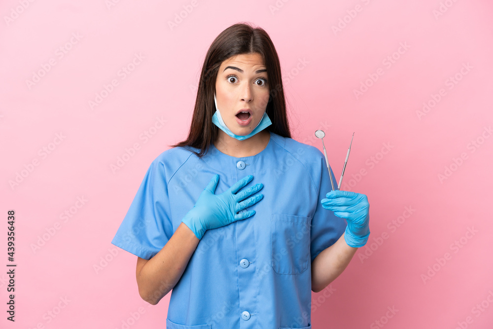 Dentist woman holding tools isolated on pink background surprised and shocked while looking right Dentist woman holding tools isolated on pink background surprised and shocked while looking right