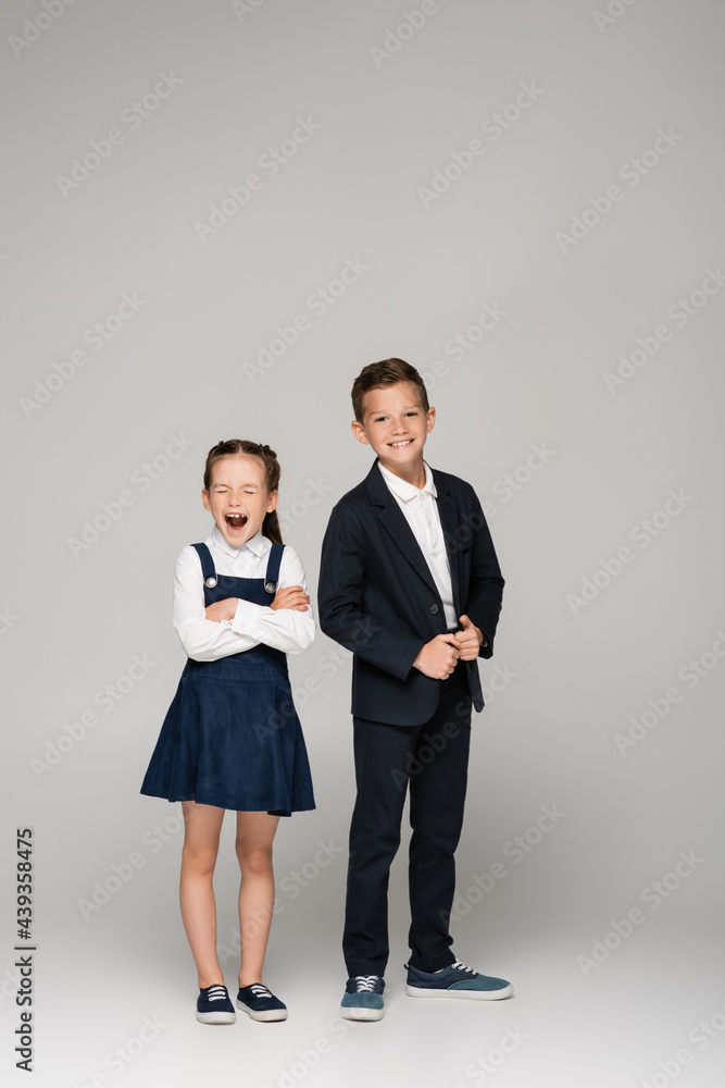 schoolgirl in dress yawning near boy in uniform on grey. schoolgirl in dress yawning near boy in uniform on grey.