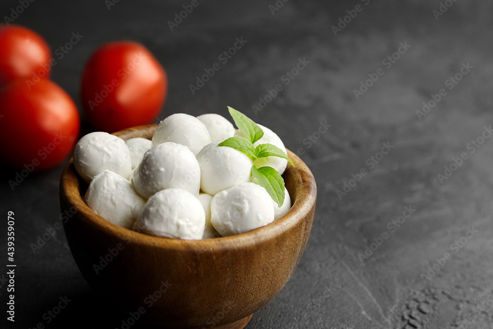Mini mozzarella cheese balls with ripe tomatoes in wooden bowl on black stony background Mini mozzarella cheese balls with ripe tomatoes in wooden bowl on black stony background