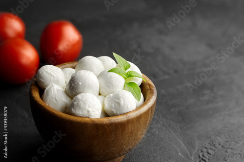 Mini mozzarella cheese balls with ripe tomatoes in wooden bowl on black stony background