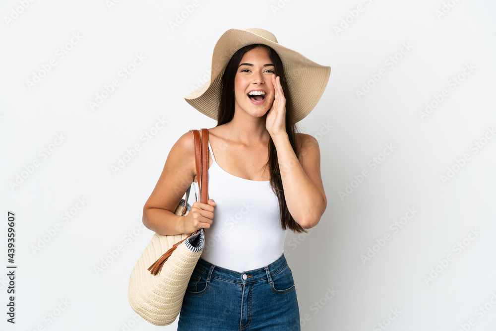 Young Brazilian woman with Pamela holding a beach bag isolated on white background shouting with mouth wide open Young Brazilian woman with Pamela holding a beach bag isolated on white background shouting with mouth wide open