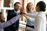 Joyful young mixed race group of employees joining hands in air, celebrating shared corporate success, involved in teambuilding activity. Happy successful multiracial colleagues giving high five.