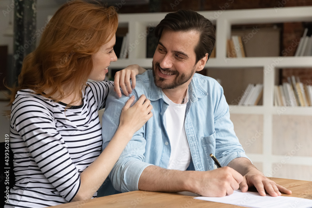 Happy bonding young family couple discussing offer, making common decision signing contract in modern office. Smiling millennial spouses feeling satisfied with new opportunity or financial deal. Happy bonding young family couple discussing offer, making common decision signing contract in modern office. Smiling millennial spouses feeling satisfied with new opportunity or financial deal.