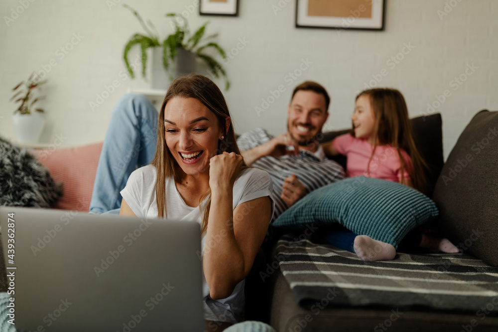 Mother sits on the floor and celebrates the good news at work, while the father and daughter cuddle. Mother sits on the floor and celebrates the good news at work, while the father and daughter cuddle.