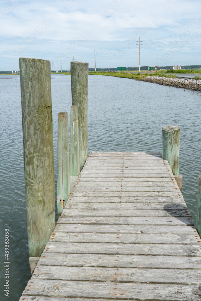 The end of a free use public man made fishing and crabbing pier, with large heavy wooden posts sunk into the soft mud bottom and wood planks making up the narrow boardwalk flooring. The end of a free use public man made fishing and crabbing pier, with large heavy wooden posts sunk into the soft mud bottom and wood planks making up the narrow boardwalk flooring.