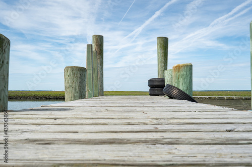 ground level view of an old public free use wooden fishing pier on a sunny summer day in a small coastal park, old tires act as bumpers on the pylons for boaters in kayaks and canoes photo