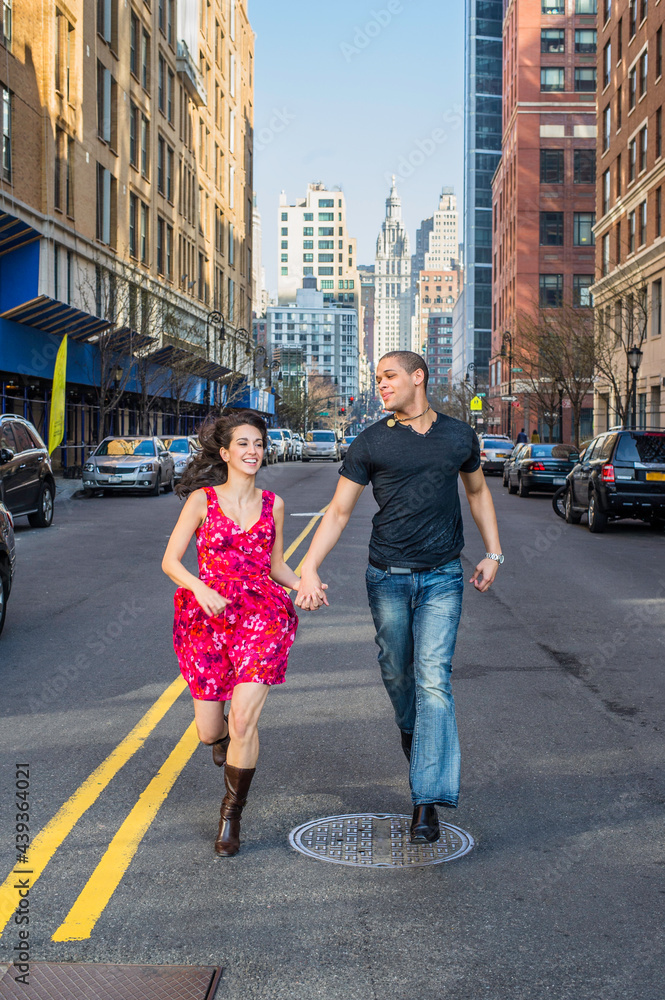 Hand in hand, a young couple is happily running on a street in a big city.