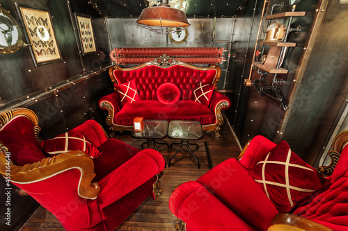 Steam punk styled dark-interior with red velvet armchairs and a sofa with pillows.