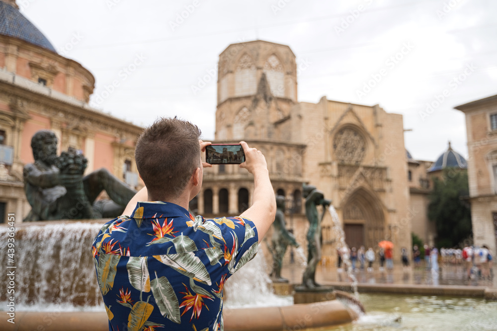 Unrecognized tourist visiting a new city using his mobile phone to take a photo of the monuments. Queen Valencia Square.