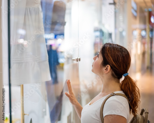 Caucasian woman looking at a shop window and dreaming about a dress.