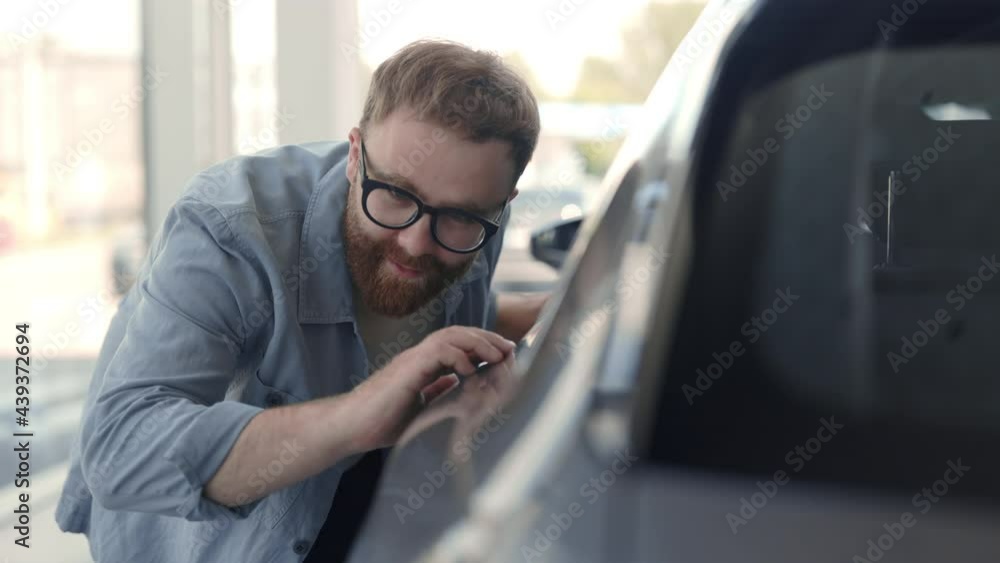 Happy man in eyeglasses touching car at modern salon Happy man in eyeglasses touching car at modern salon