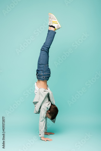 Fototapeta boy in denim jeans doing handstand on blue.