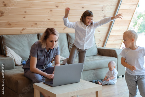 Serious woman using laptop near playing children at home