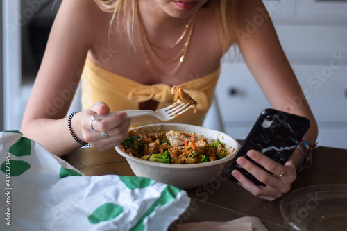 Young woman eating take out food and using mobile phone