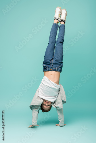 Tablou pe pânză happy boy in denim jeans doing handstand on blue.