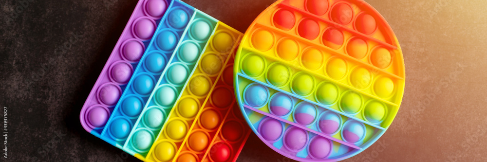 kids anti stress sensory pop it or simple dimple fidget push toys on a black table or floor background. popit rainbow hue bright color, trend 2021 year. top view, flat lay. banner. flare kids anti stress sensory pop it or simple dimple fidget push toys on a black table or floor background. popit rainbow hue bright color, trend 2021 year. top view, flat lay. banner. flare