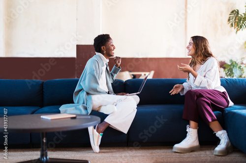 Happy diverse coworkers talking on sofa