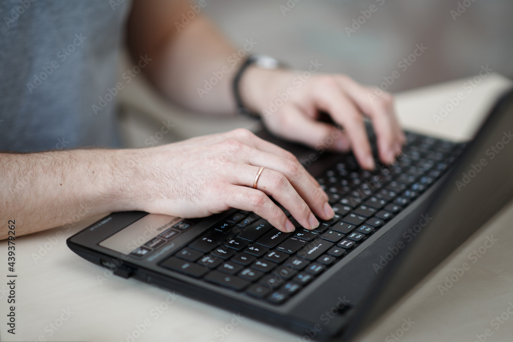 in a bright room, a 35-year-old man works at a desk, with a laptop, in a gray T-shirt, a man works remotely, headphones on his head, a notebook, a pen on the table, an office at home in a bright room, a 35-year-old man works at a desk, with a laptop, in a gray T-shirt, a man works remotely, headphones on his head, a notebook, a pen on the table, an office at home