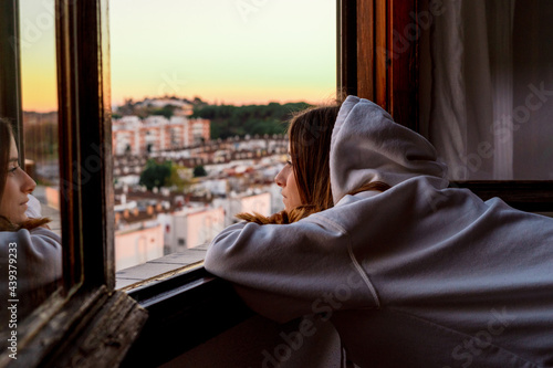 Teenager girl looking at the city from her home window photo