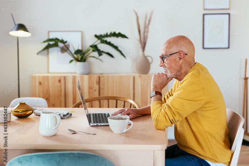 Pensive senior man browsing laptop in morning Pensive senior man browsing laptop in morning