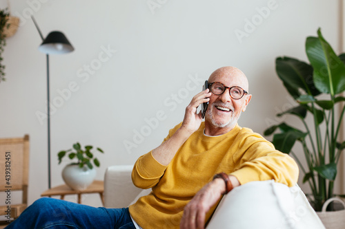 Happy aged male speaking on smartphone on couch photo
