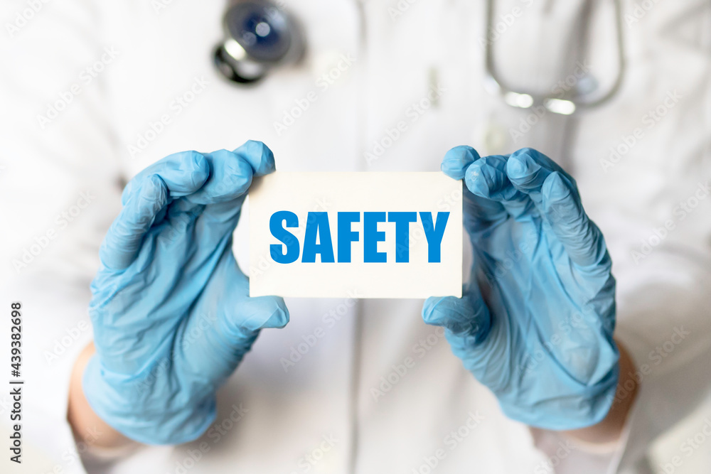 A medical worker in gloves holds a card with the words SAFETY. Medical concept A medical worker in gloves holds a card with the words SAFETY. Medical concept