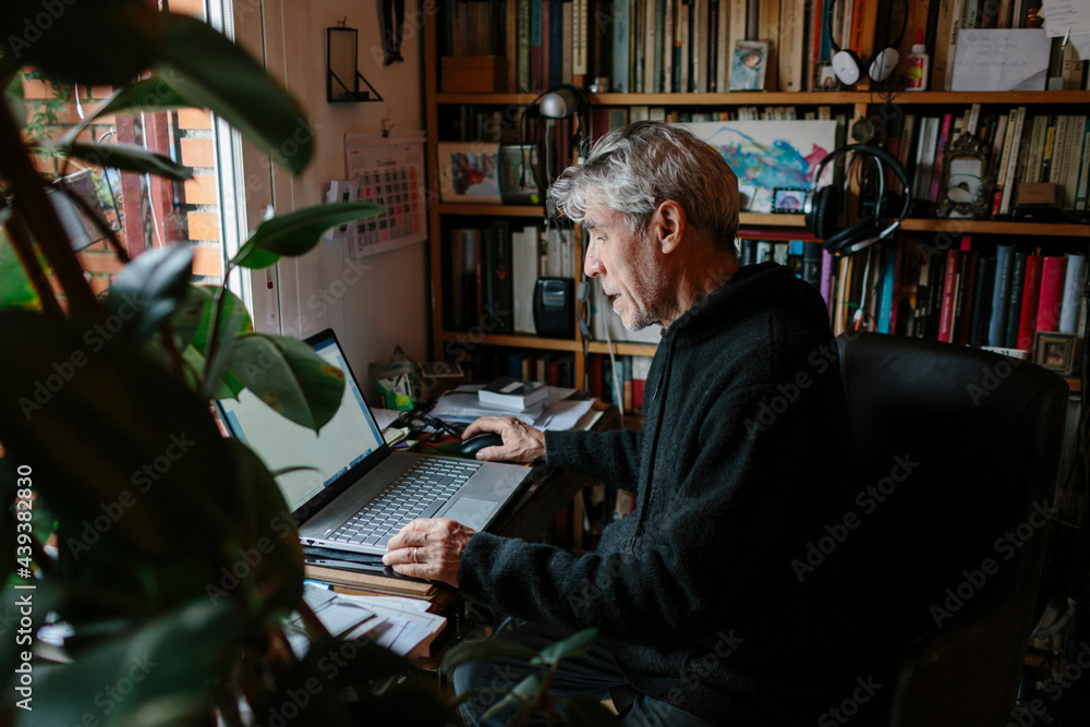 Man at his home office checking information on his laptop. Man at his home office checking information on his laptop.