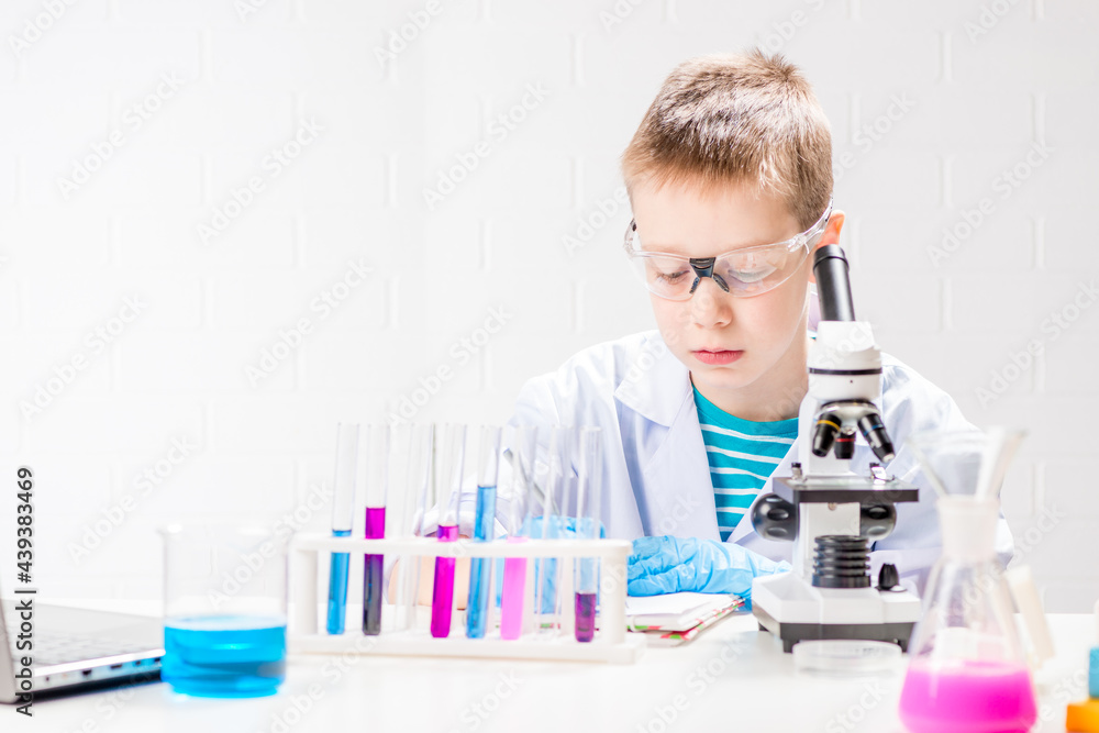 A schoolboy with a microscope examines chemicals in test tubes, conducts experiments - a portrait on a white background. Concept for the study of coronavirus in the laboratory A schoolboy with a microscope examines chemicals in test tubes, conducts experiments - a portrait on a white background. Concept for the study of coronavirus in the laboratory