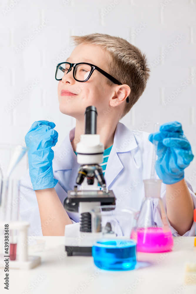 A schoolboy with a microscope examines chemicals in test tubes, conducts experiments - a portrait on a white background. Concept for the study of coronavirus in the laboratory A schoolboy with a microscope examines chemicals in test tubes, conducts experiments - a portrait on a white background. Concept for the study of coronavirus in the laboratory