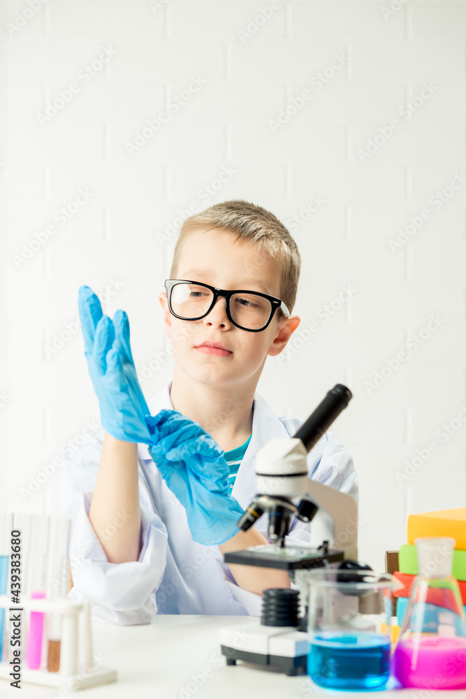 A schoolboy with a microscope examines chemicals in test tubes, conducts experiments - a portrait on a white background. Concept for the study of coronavirus in the laboratory A schoolboy with a microscope examines chemicals in test tubes, conducts experiments - a portrait on a white background. Concept for the study of coronavirus in the laboratory