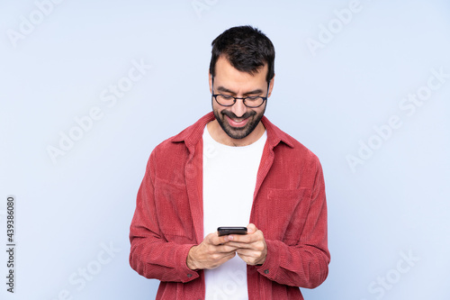 Young caucasian man wearing corduroy jacket over blue background sending a message with the mobile