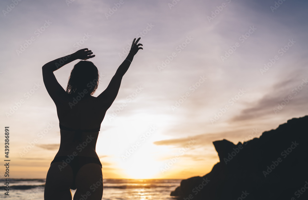 Slim woman with arms raised in picturesque sunset