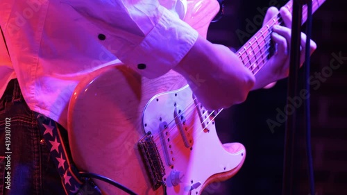 Man rhythm guitarist playing electric guitar on a rock concert in a club. Red lighting, hands closeup.