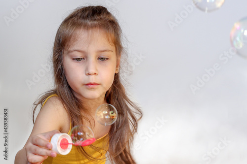 Little girl with long blond hair plays with soap bubbles