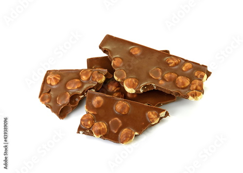 A broken pieces of chocolate with hazelnuts isolated on white background. Milk chocolate tiles with nuts isolated on white.