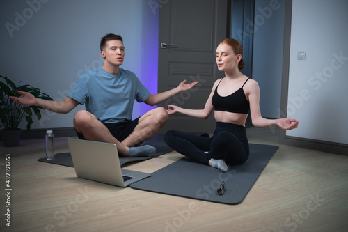 The newlyweds home room for yoga classes, they meditate on the floor under a video with relaxing music from a laptop